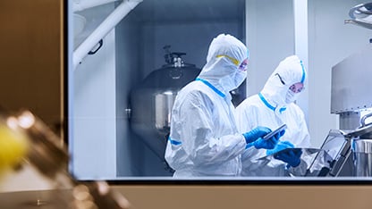Scientists in cleanroom suits using digital tablets during a laboratory experiment