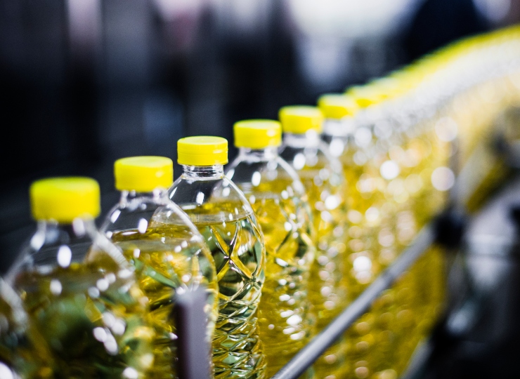 Bottles of oil moving along a conveyor belt, emphasizing the significance of food contact testing for packaging materials