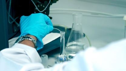 A person in a lab coat and blue gloves tests cosmetics for heavy metals in a laboratory setting.