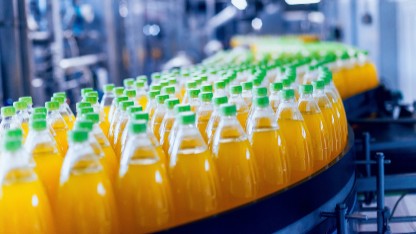 Bottles of orange juice moving along a conveyor belt, emphasizing safety testing for non-intentionally added substances in packaging